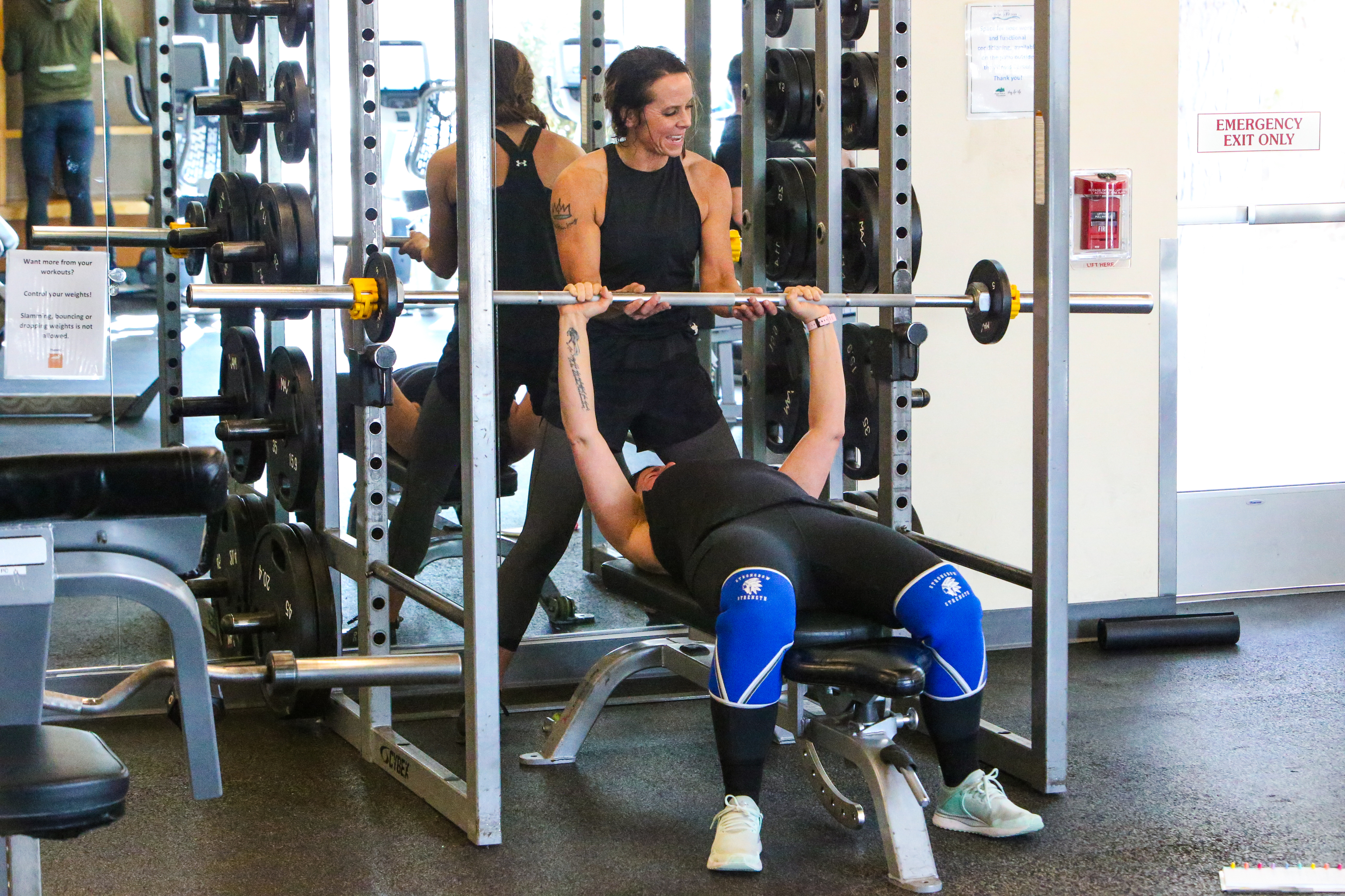 A woman is spotting another woman while bench pressing at Juniper fitness center