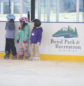 children learning to ice skate in front of an ice rink dasher board at The Pavilion.