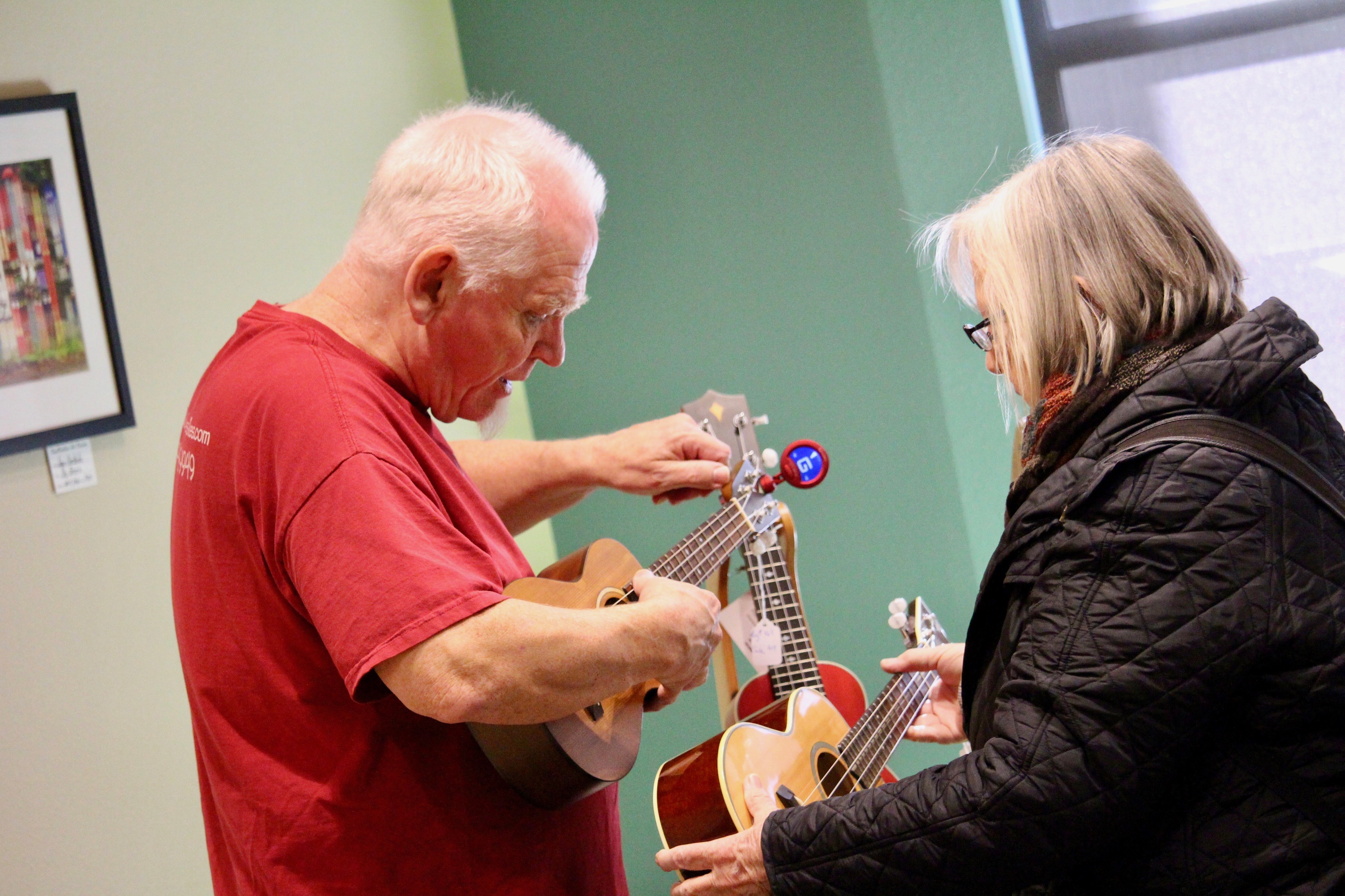 A man showing a woman how to play a ukulele