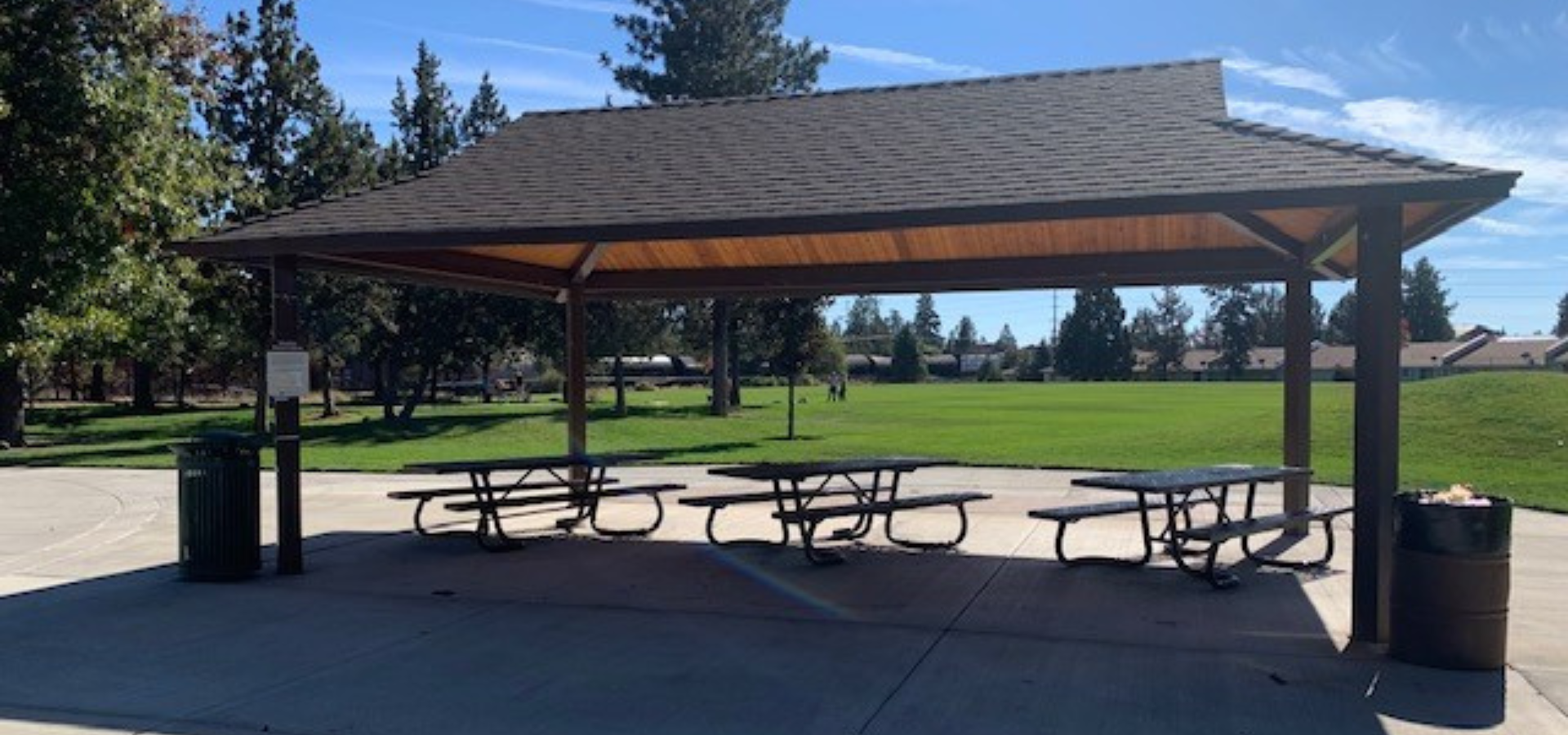 picnic shelter at Kiwanis park covering park benches in the shade with sunny green lawn in thebackground