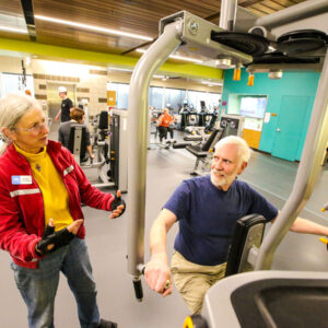 A volunteer assists a patron with using one of the fitness machines at Larkspur.