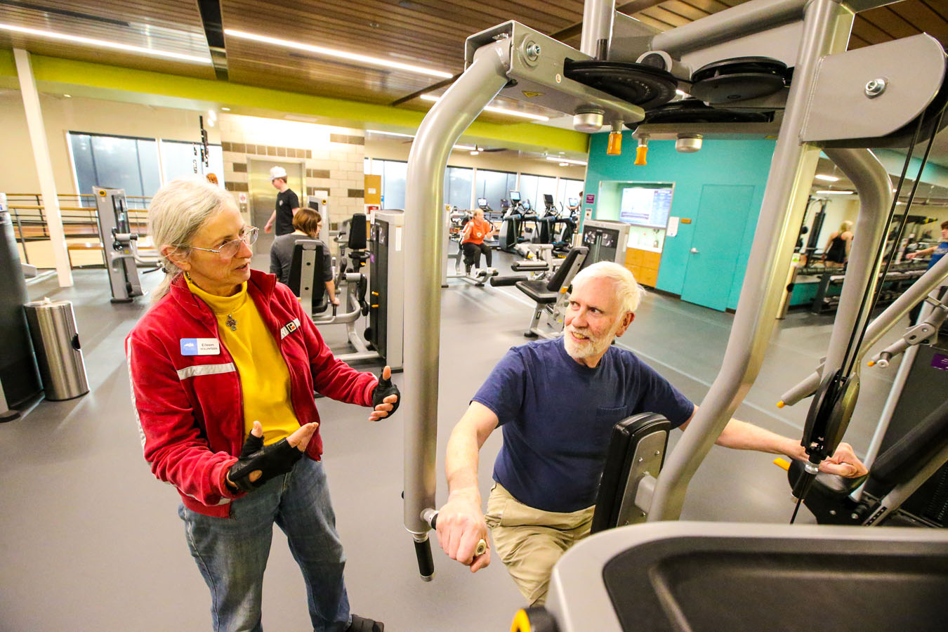 A volunteer assists a patron with using one of the fitness machines at Larkspur.