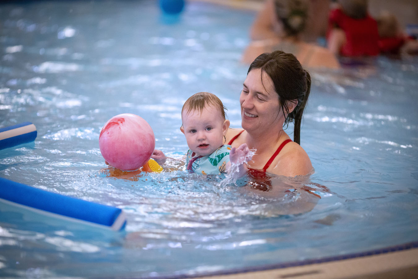 Mother playing with her young child in the pool at swim lessons.