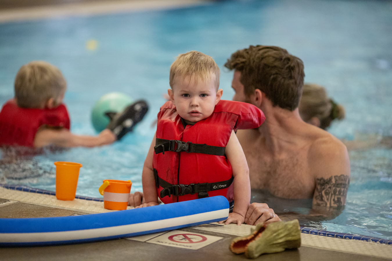 A young child looks at the camera wearing a floatation vest in the pool.