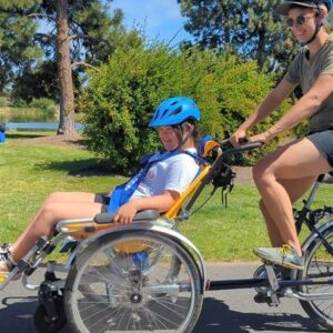 Photo of young girl and guardian on an adaptive bicycle