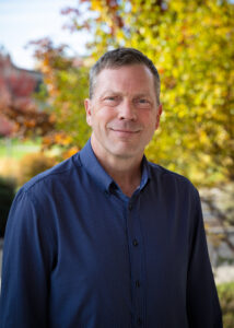 Photograph of Cary Schneider looking directly forward with trees in the background.