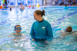 Child with swimming goggles and a BPRD swim instructor talk in the pool.